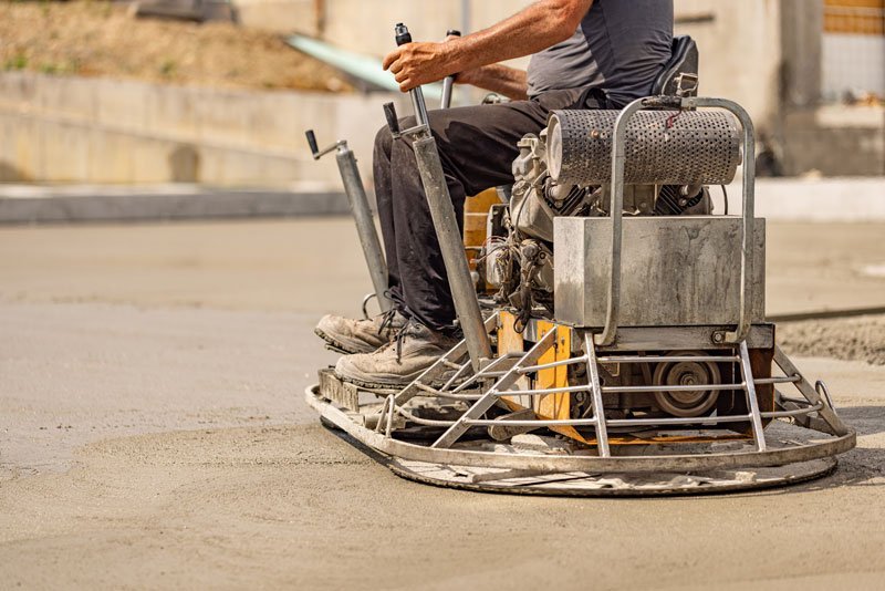 Operador utilizando una allanadora de operador a bordo para pulir y nivelar un piso de concreto fresco en obra.